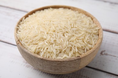 Photo of Raw rice in bowl on light wooden table, closeup