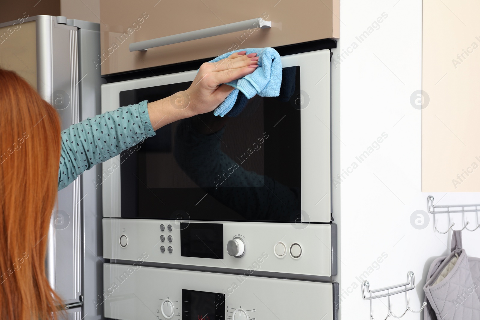 Photo of Woman cleaning oven with rag in kitchen