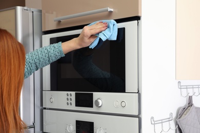 Woman cleaning oven with rag in kitchen