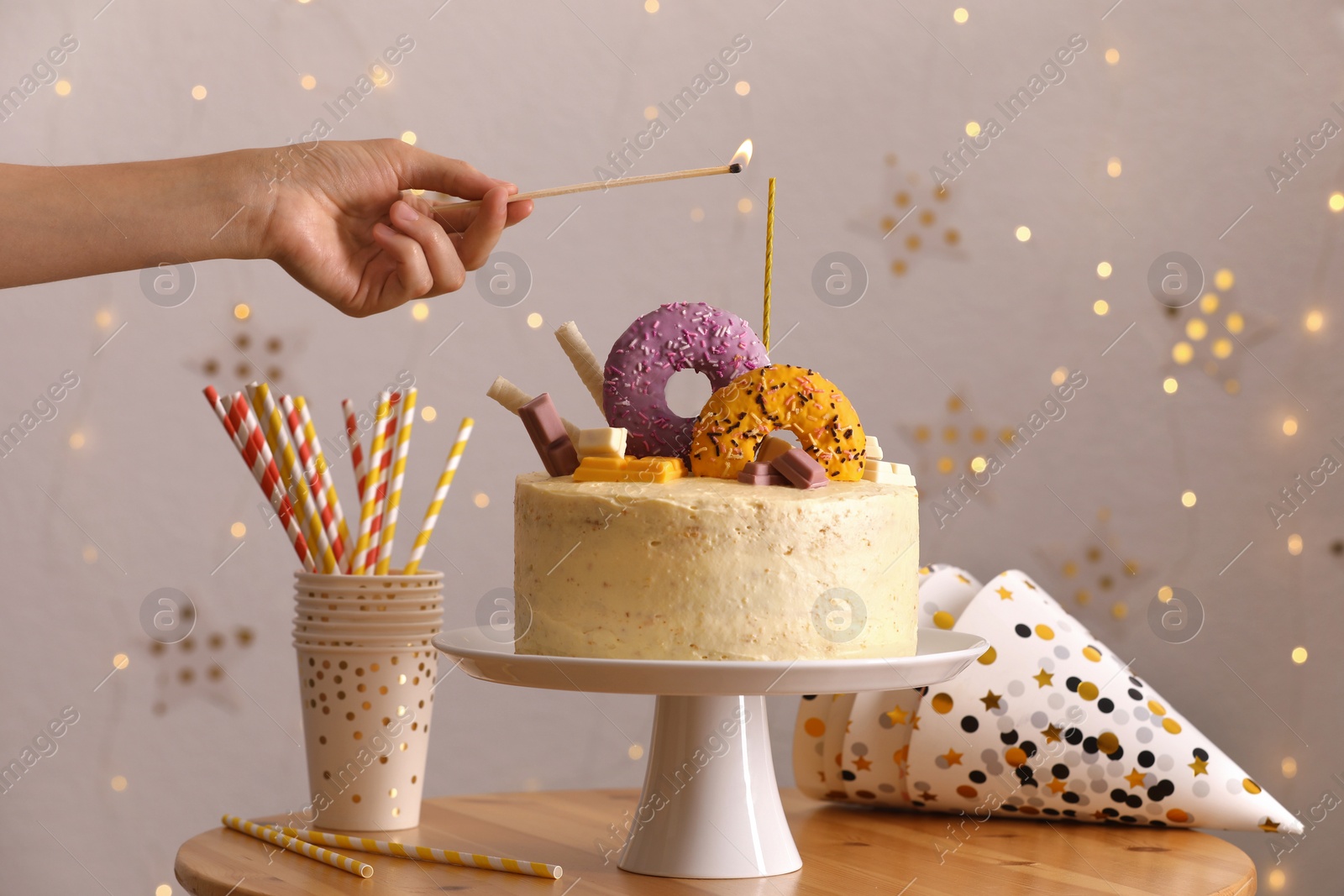 Photo of Woman lighting candle on delicious cake decorated with sweets at wooden table, closeup