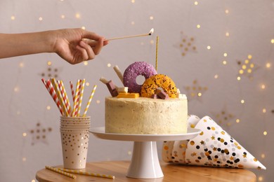 Photo of Woman lighting candle on delicious cake decorated with sweets at wooden table, closeup