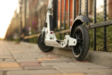 Modern electric kick scooter near metal fence outdoors, closeup