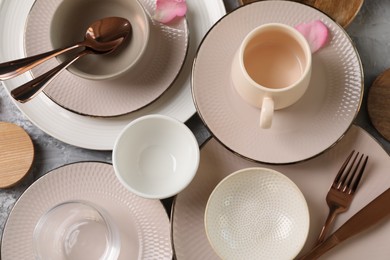 Stylish table setting. Dishes, cutlery, cup and petals on grey surface, flat lay