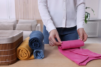 Photo of Woman rolling shirt at table in room, closeup. Organizing clothes