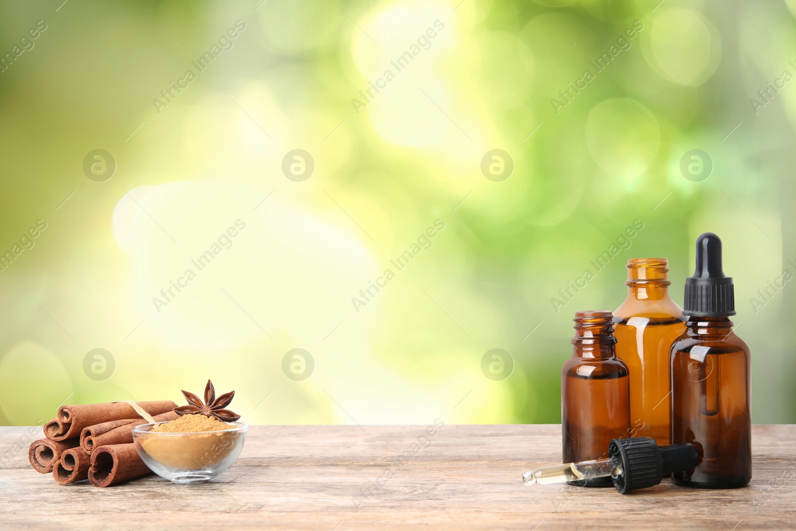 Image of Bottles of essential oil, cinnamon sticks and powder on wooden table against blurred background. Space for text