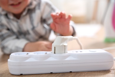 Photo of Little child playing with power strip and plug on floor indoors, closeup. Dangerous situation