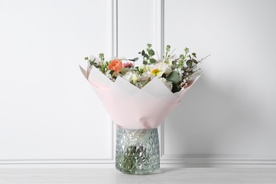 Photo of Bouquet of beautiful flowers in vase on wooden table against white wall