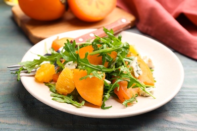 Photo of Delicious persimmon salad served on light blue wooden table, closeup