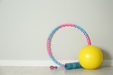 Photo of Hula hoop, exercise ball, yoga mat and dumbbells near light wall in gym. Space for text
