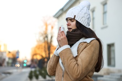 Photo of Woman with tissue blowing runny nose outdoors, space for text. Cold symptom