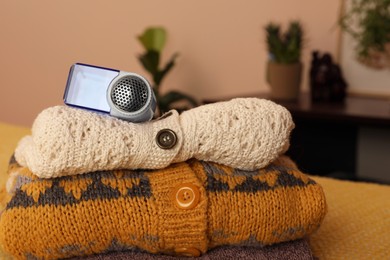 Photo of Modern fabric shaver and knitted clothes on orange blanket indoors, closeup