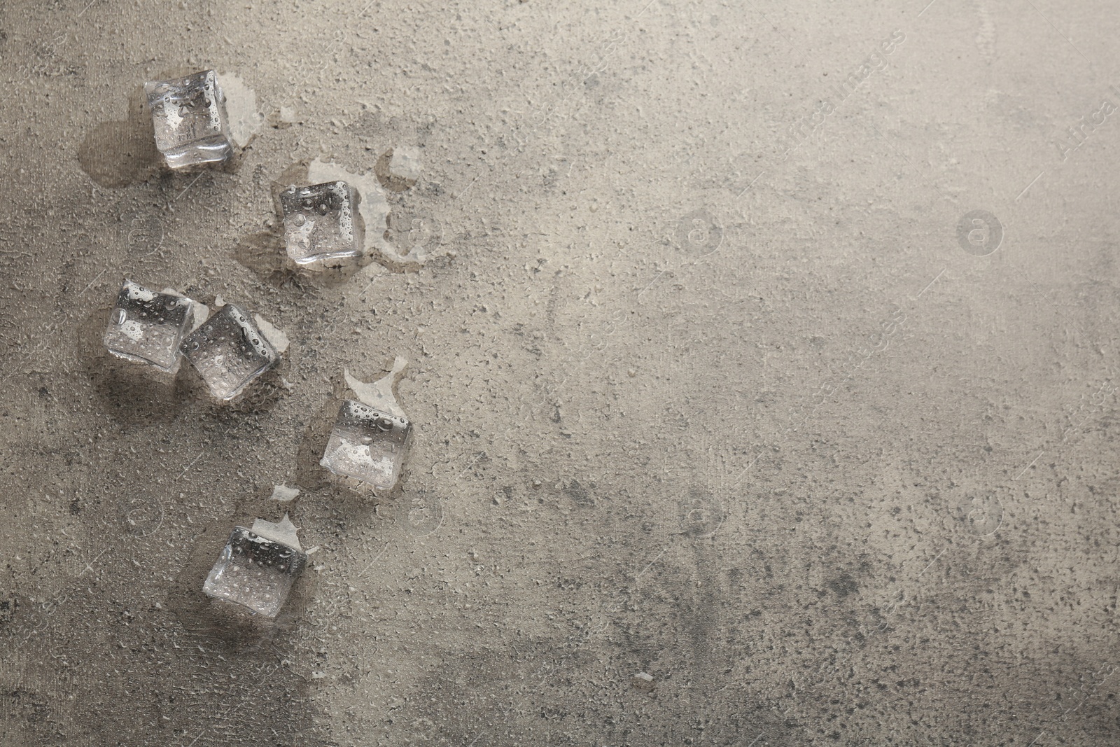 Photo of Melting ice cubes and water drops on grey textured table, flat lay. Space for text