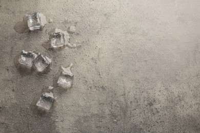 Photo of Melting ice cubes and water drops on grey textured table, flat lay. Space for text