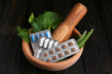 Photo of Mortar with fresh green herbs and pills on wooden table