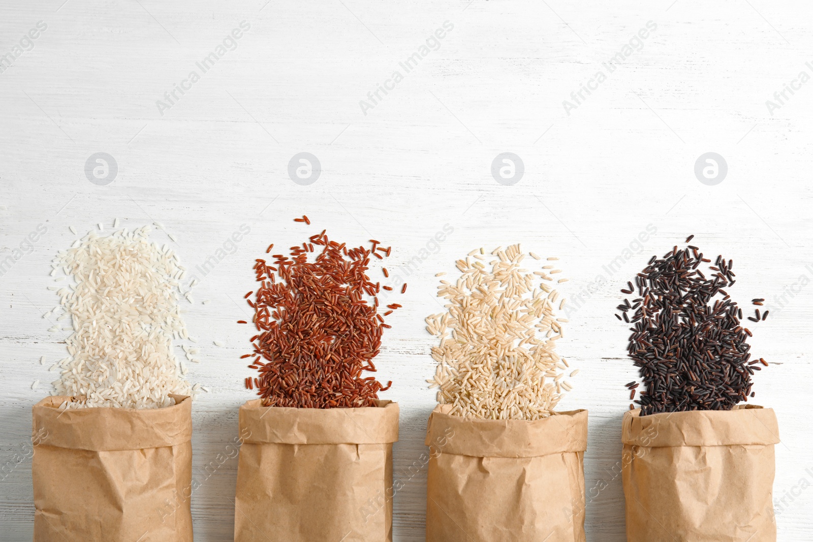 Photo of Paper bags with different types of rice on white wooden background, top view. Space for text