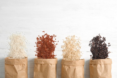 Paper bags with different types of rice on white wooden background, top view. Space for text