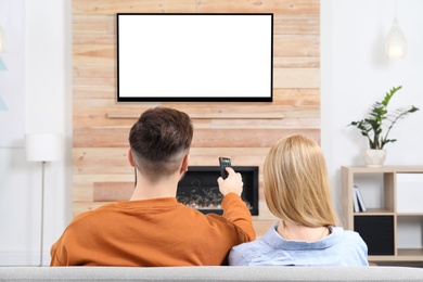 Photo of Couple watching TV on sofa in living room with decorative fireplace