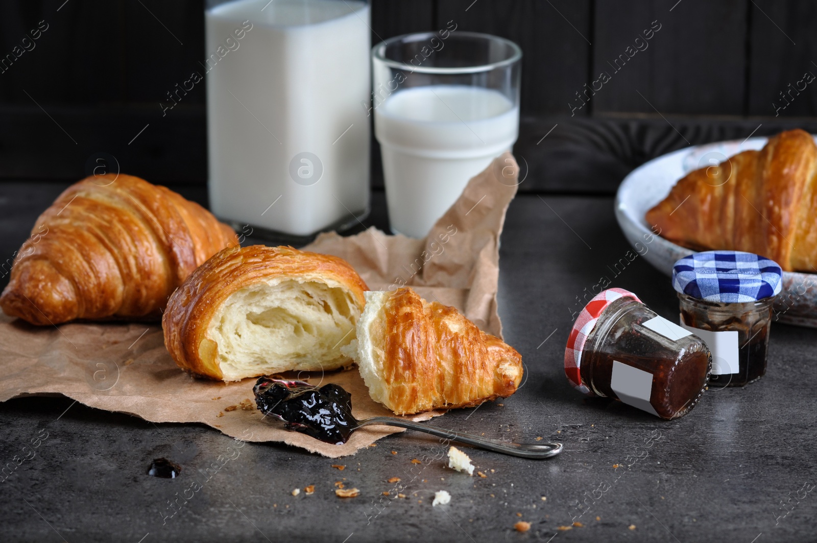 Photo of Tasty fresh croissants with jam and milk on grey table