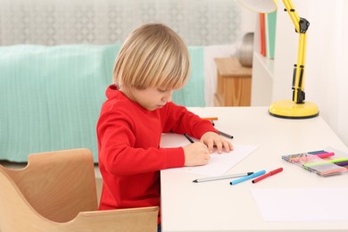 Little boy drawing at desk in room. Home workplace