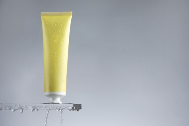 Photo of Moisturizing cream in tube on glass with water drops against grey background. Space for text