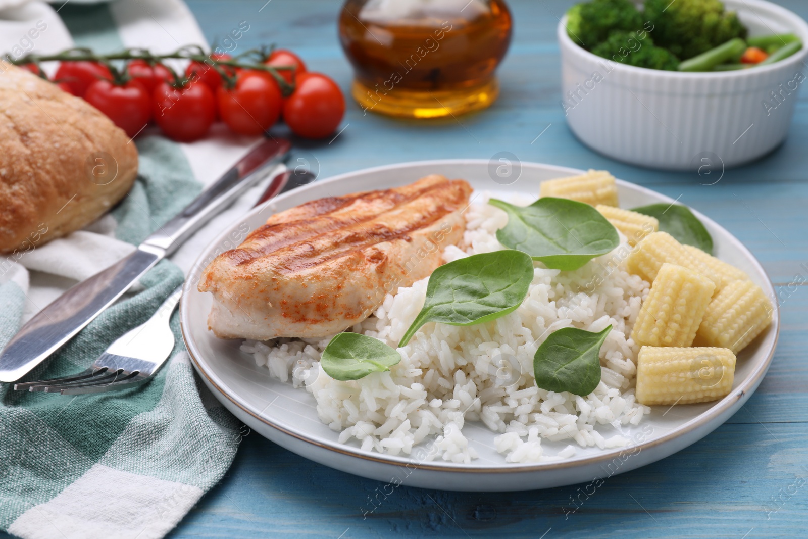 Photo of Grilled chicken breast and rice served with vegetables on light blue wooden table