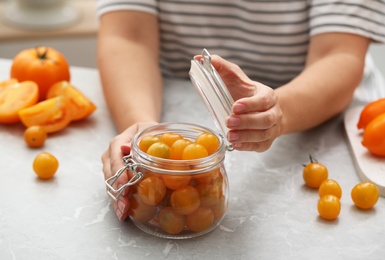 Woman pickling glass jar of yellow tomatoes at light kitchen table, closeup