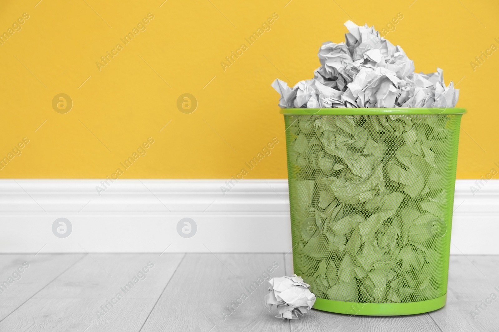 Photo of Metal bin with crumpled paper against color wall, space for text