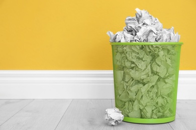 Photo of Metal bin with crumpled paper against color wall, space for text