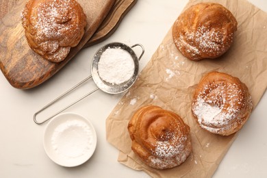Photo of Delicious profiteroles with powdered sugar on white table, flat lay