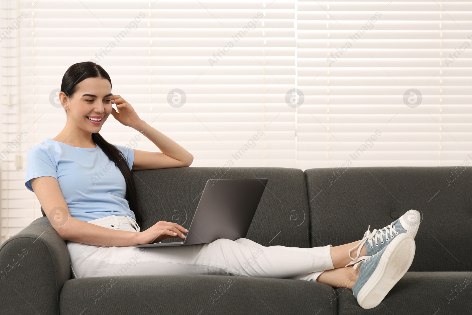 Photo of Happy woman working with laptop on sofa at home