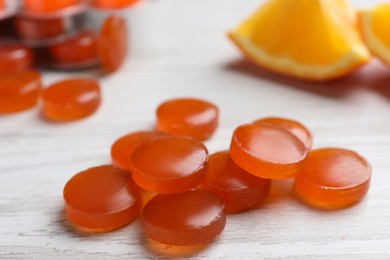 Photo of Many orange cough drops on white wooden table, closeup