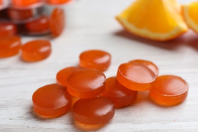 Many orange cough drops on white wooden table, closeup