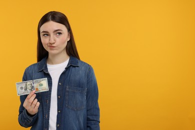 Photo of Sad woman with dollar banknote on orange background, space for text