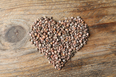 Photo of Heart made of raw radish seeds on wooden background, top view. Vegetable planting