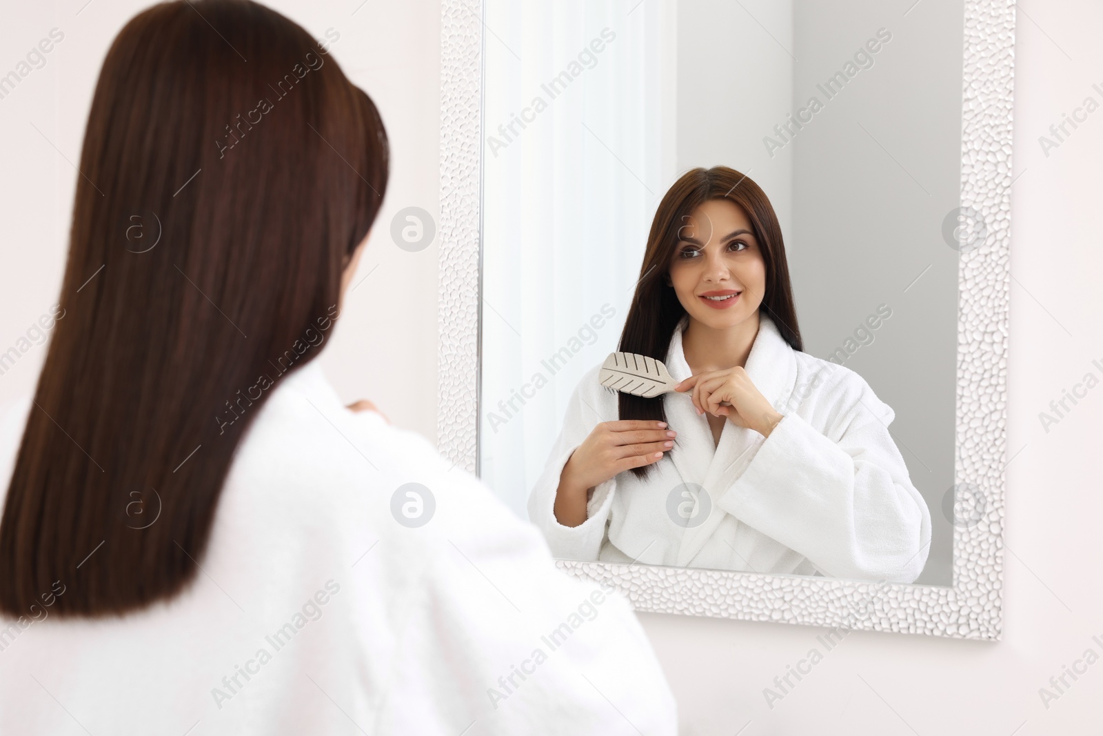 Photo of Beautiful woman brushing her hair near mirror indoors