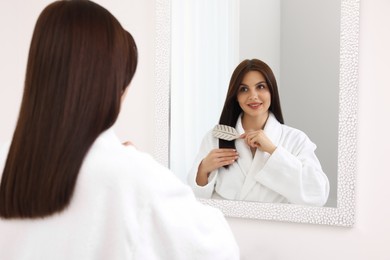 Photo of Beautiful woman brushing her hair near mirror indoors