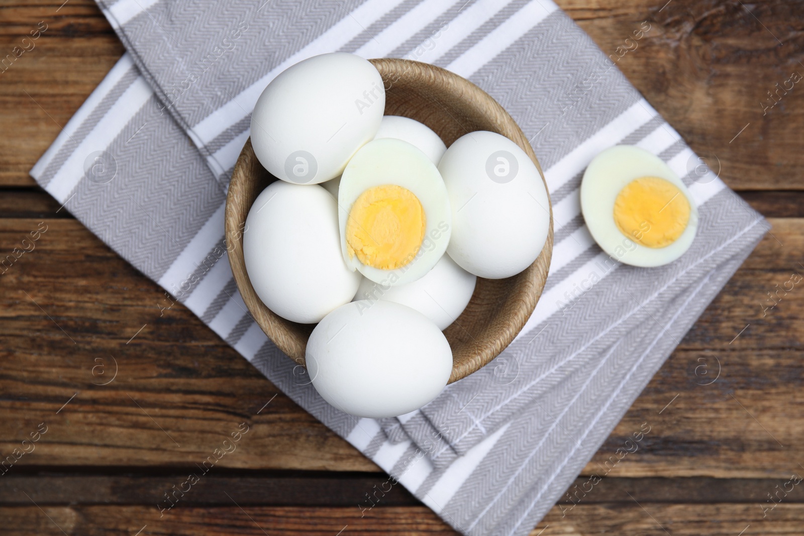 Photo of Bowl with hard boiled eggs and kitchen towel on wooden table, top view
