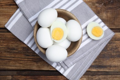 Bowl with hard boiled eggs and kitchen towel on wooden table, top view