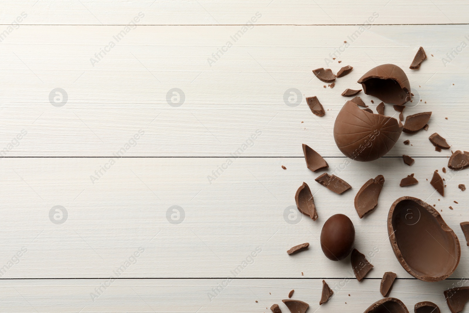 Photo of Broken and whole chocolate eggs on white wooden table, flat lay. Space for text