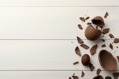 Photo of Broken and whole chocolate eggs on white wooden table, flat lay. Space for text