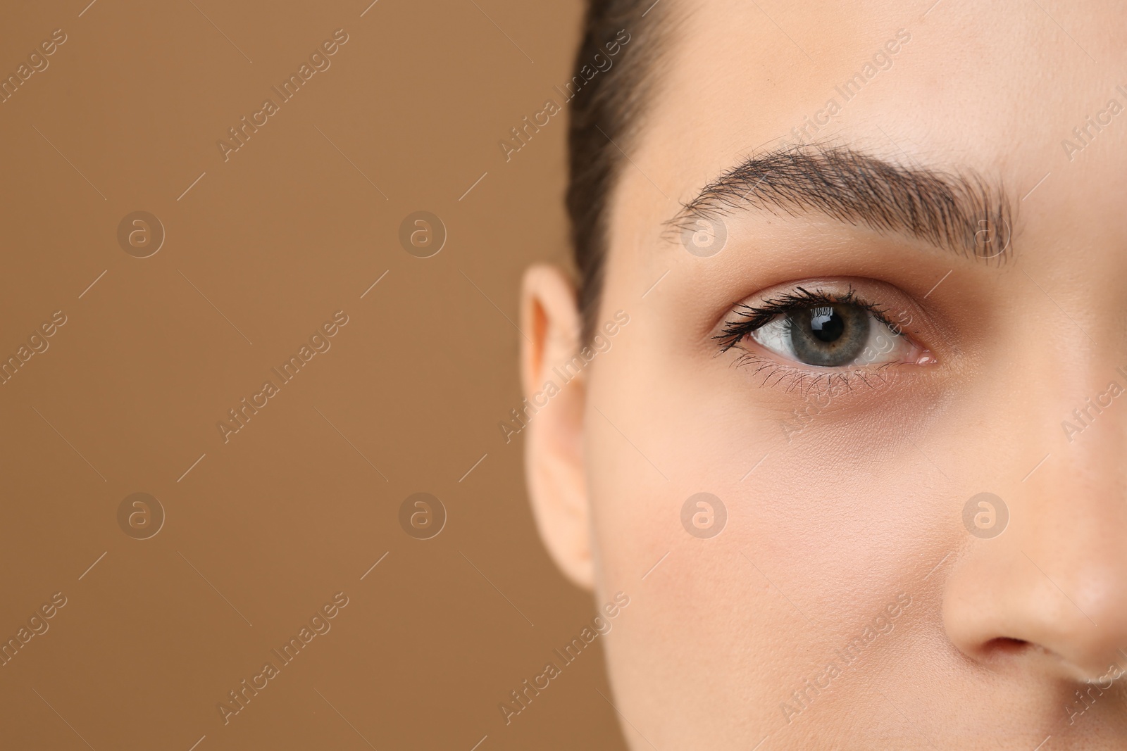 Photo of Young woman with perfect eyebrows on brown background, closeup. Space for text