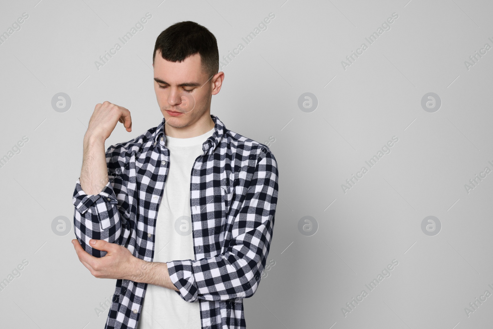 Photo of Man suffering from pain in his elbow on light background, space for text. Arthritis symptoms