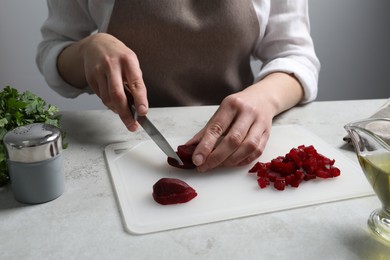 Woman cutting boiled beetroot at white table, closeup. Cooking vinaigrette salad