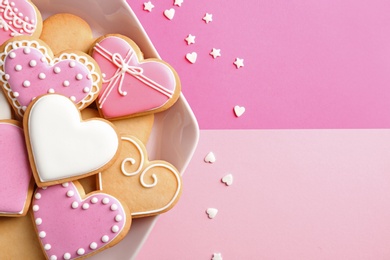 Photo of Plate with decorated heart shaped cookies and candy confetti on color background, top view. Space for text