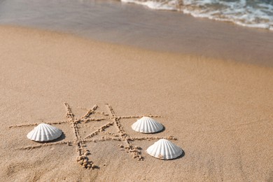 Photo of Playing Tic tac toe game with shells on sand near sea. Space for text