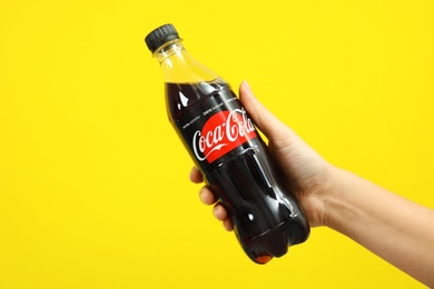 Photo of MYKOLAIV, UKRAINE - NOVEMBER 14, 2018: Woman holding bottle of Coca-Cola on color background