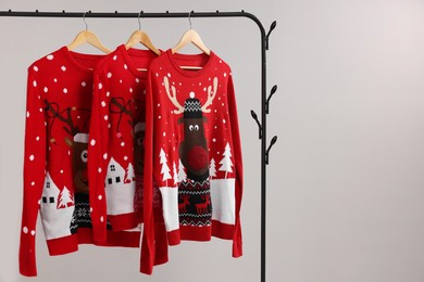 Photo of Rack with different Christmas sweaters on light background, space for text