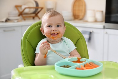 Cute little baby eating food in high chair at kitchen