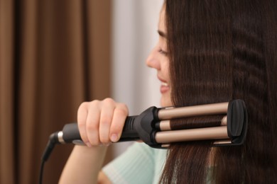 Photo of Young woman using modern curling iron indoors, focus on device