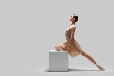 Photo of Young ballerina practicing dance moves on cube against white background. Space for text
